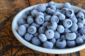Close-up of frozen blueberries in a white bowl on a rustic wooden table, highlighting texture.
