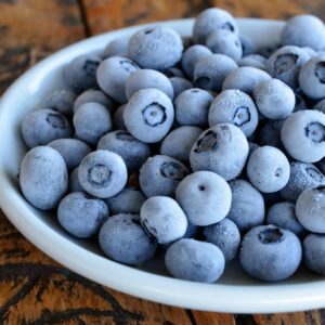 Close-up of frozen blueberries in a white bowl on a rustic wooden table, highlighting texture.